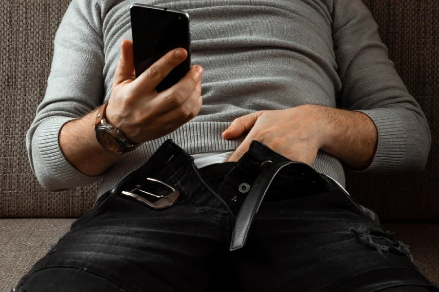 Man unbuckling his belt with phone in hand