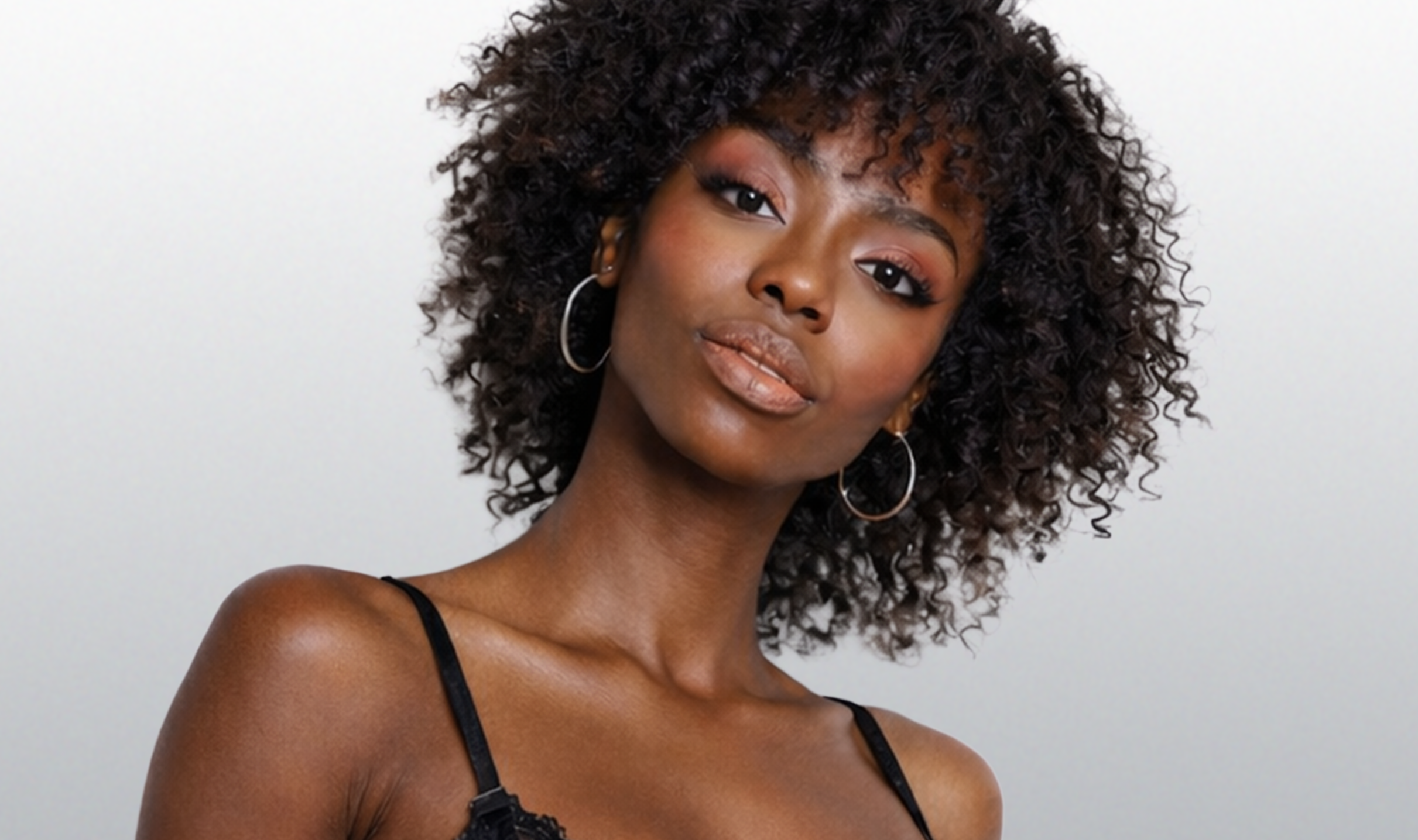 Woman with curly hair wearing hoop earrings against a plain background