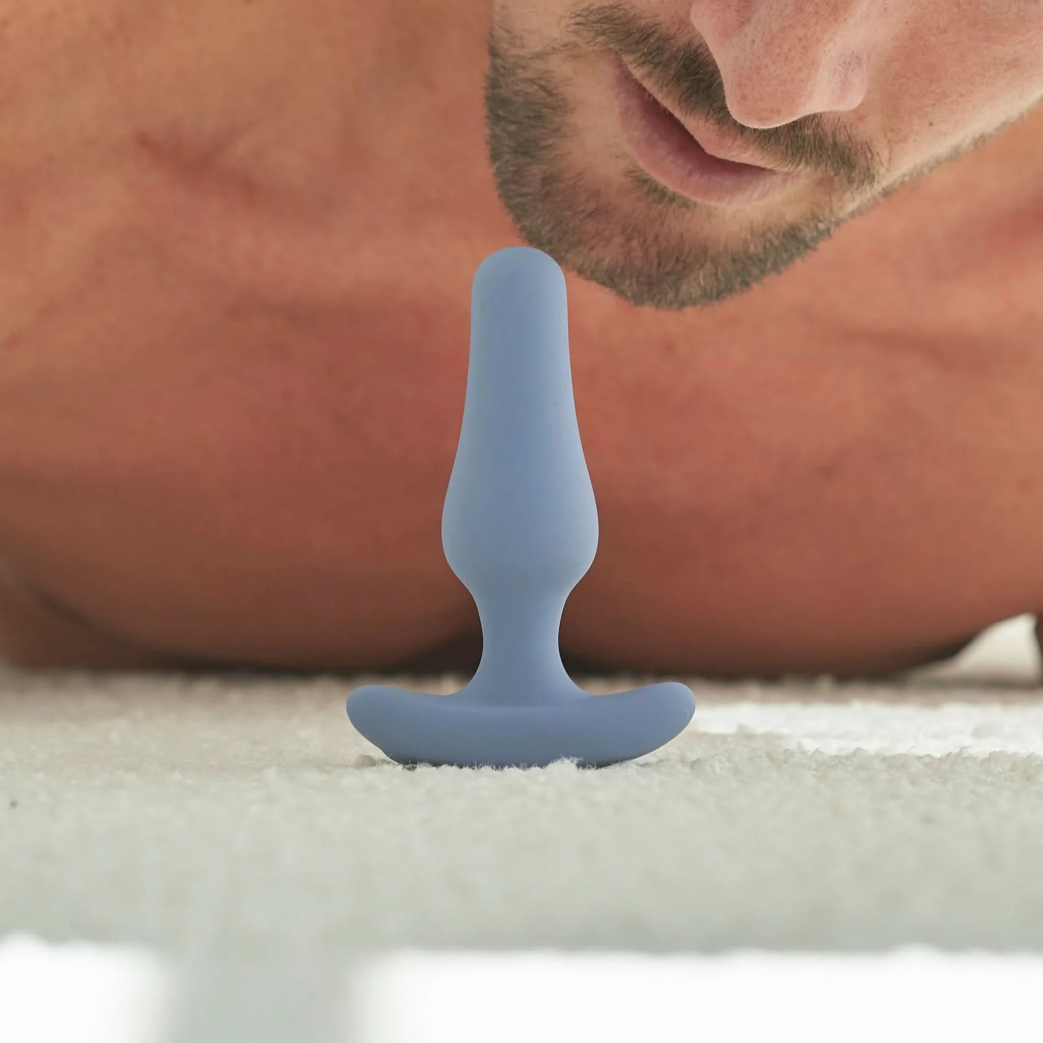 A shirtless man lies on the floor near a blue JIMMYJANE® Dia® with Remote, featuring seven vibration modes, standing upright.