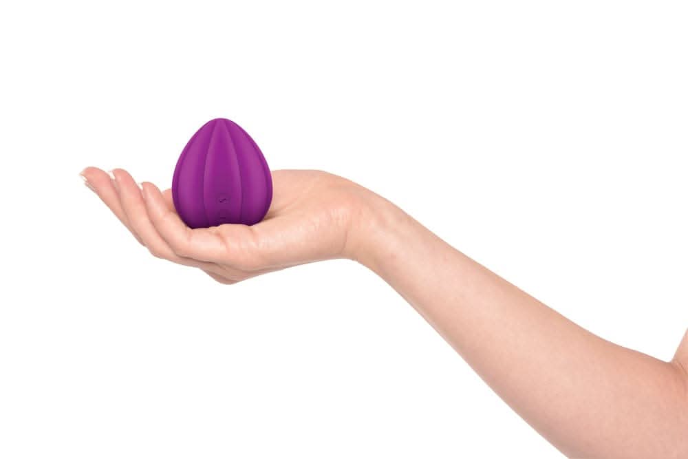 A hand holding the JIMMYJANE® Love Pods™ Om, a small, purple, egg-shaped vibrator for clitoral stimulation, against a white background.