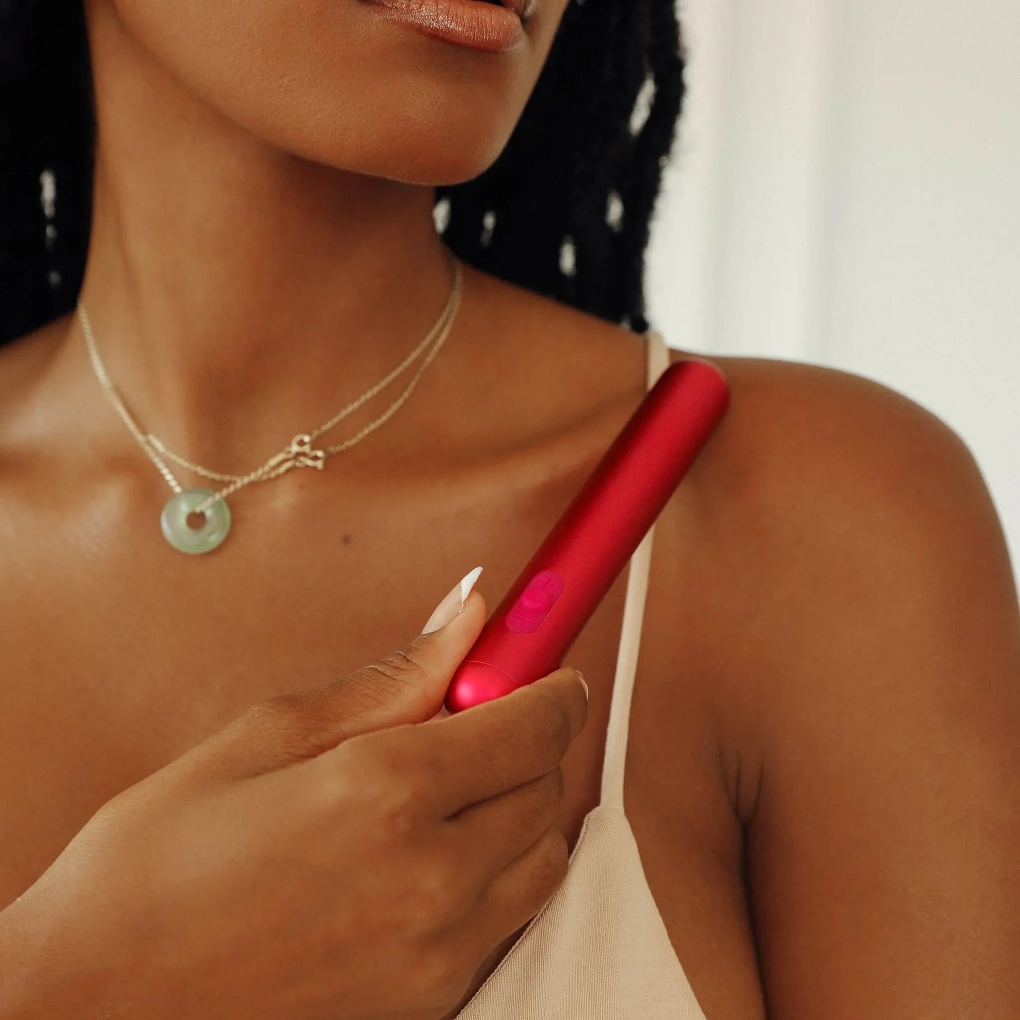 A woman in a beige top holds the JIMMYJANE® Chroma™ bullet vibrator, known for its sleek, waterproof design, against her collarbone.