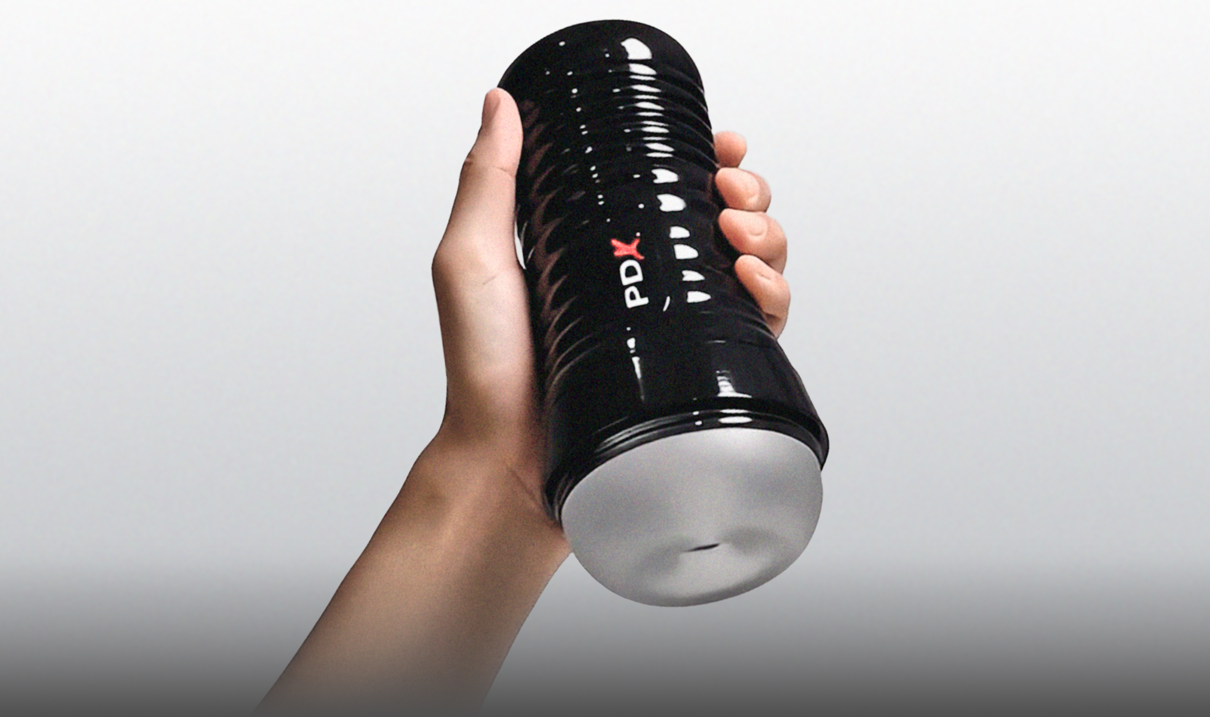 Hand holding a black and white container with 'PDX' Stroker against a gray background