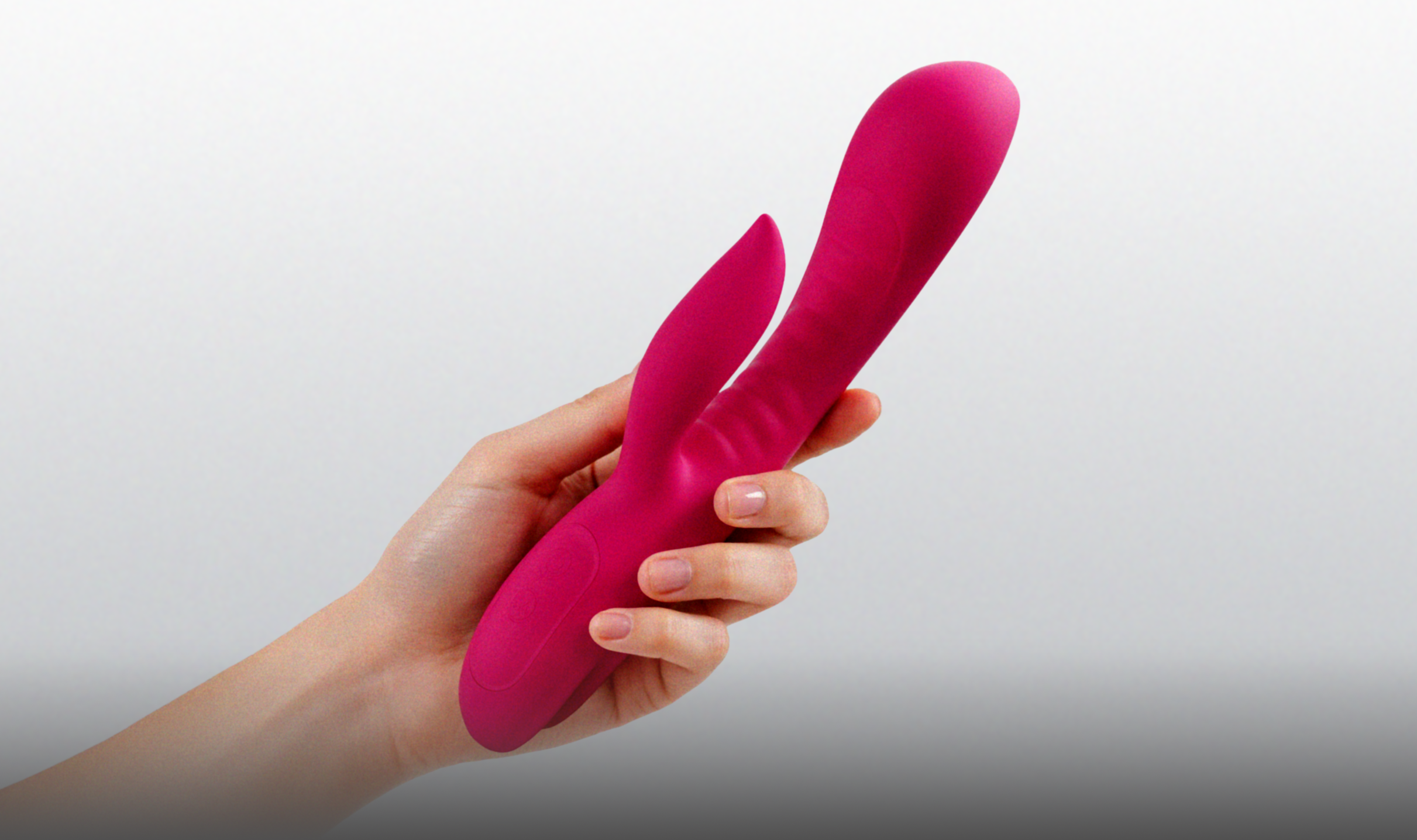 Hand holding a pink silicone rabit vibrator against a gray background