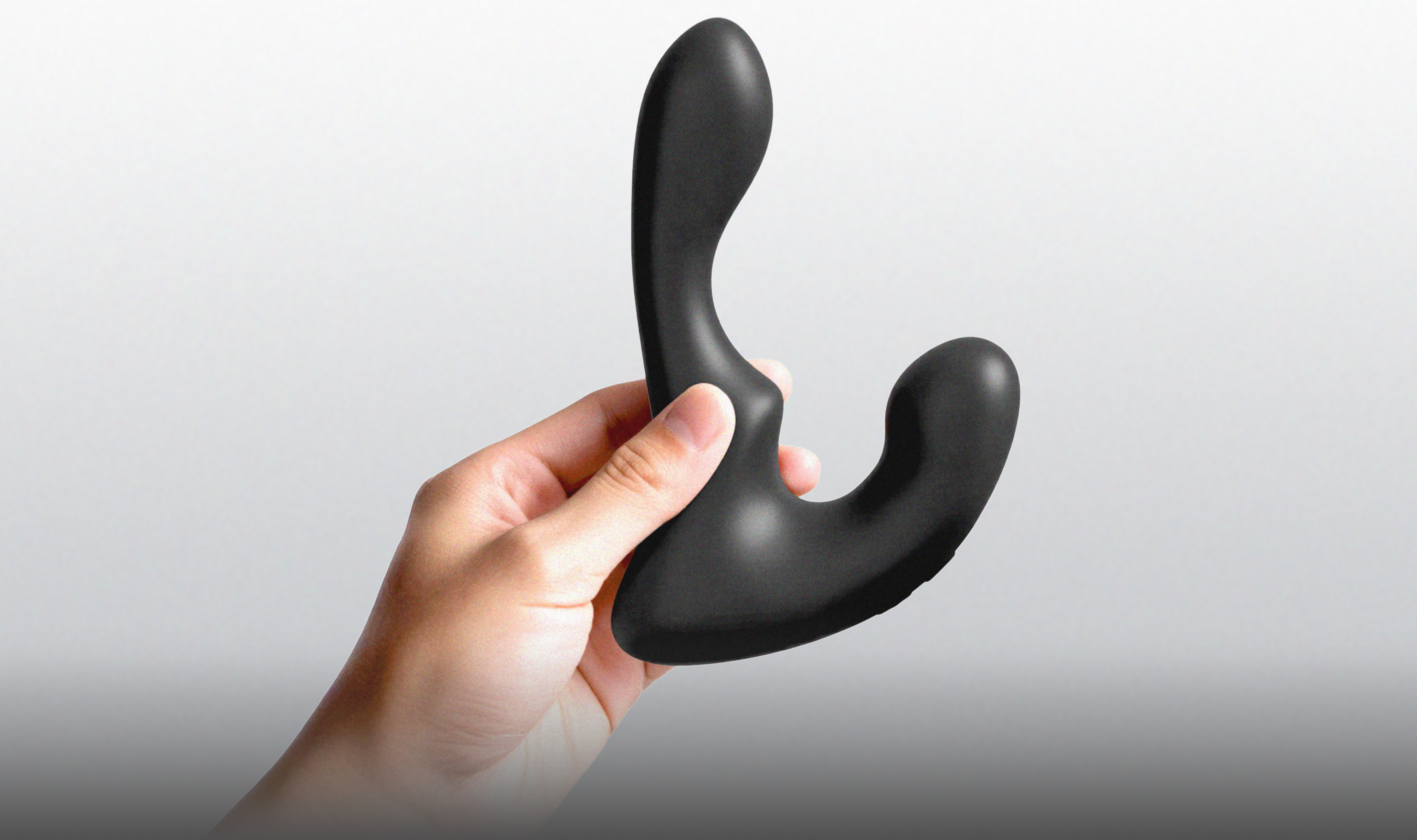 Black anal vibrator held in a hand against a light gray background