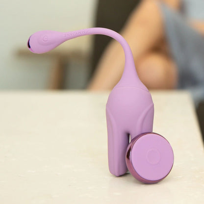 A purple JIMMYJANE® Form 2® Kegel Trainer with dual vibrating motors and a flexible stem rests on a table, while a person appears blurred in the background.