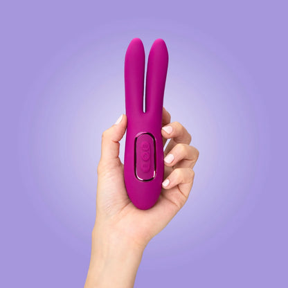 A hand holds the JIMMYJANE® Solis™ Ascend 2® Pro, showcasing its flexible dual ear design for intense stimulation, set against a light purple background.