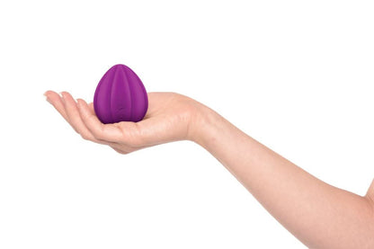 A hand holding the JIMMYJANE® Love Pods™ Om, a small, purple, egg-shaped vibrator for clitoral stimulation, against a white background.